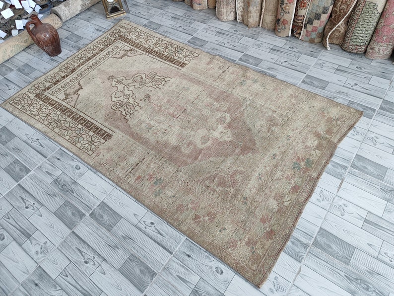 May include: A beige prayer rug with a brown floral pattern and a central design. The rug has a worn, vintage look.