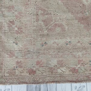 May include: A vintage rug with a faded pink and beige floral pattern. The rug has a frayed edge and a woven texture.