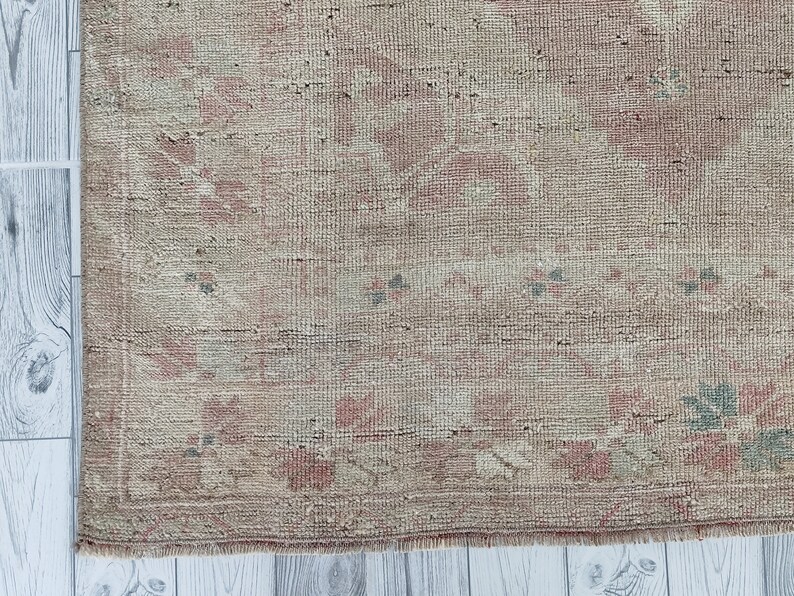 May include: A vintage rug with a faded pink and beige floral pattern. The rug has a frayed edge and a woven texture.