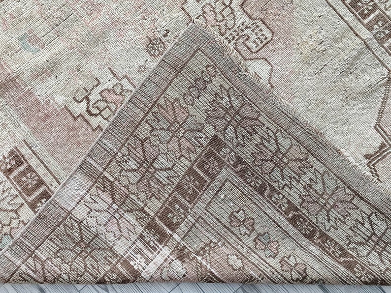 May include: A close-up of a vintage rug with a faded pink and brown geometric pattern. The rug has a worn and distressed look, with frayed edges and a soft texture.