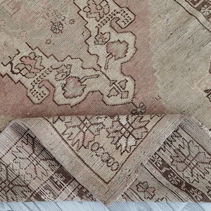 May include: A vintage rug with a light brown and pink color scheme. The rug has a floral pattern with intricate details. The rug is folded in half, showing the underside of the rug.