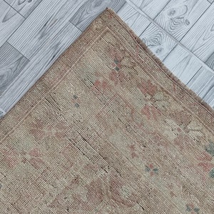 May include: A vintage rug with a faded floral pattern in shades of pink, green, and beige. The rug has a worn, distressed look and is made of a natural fiber.