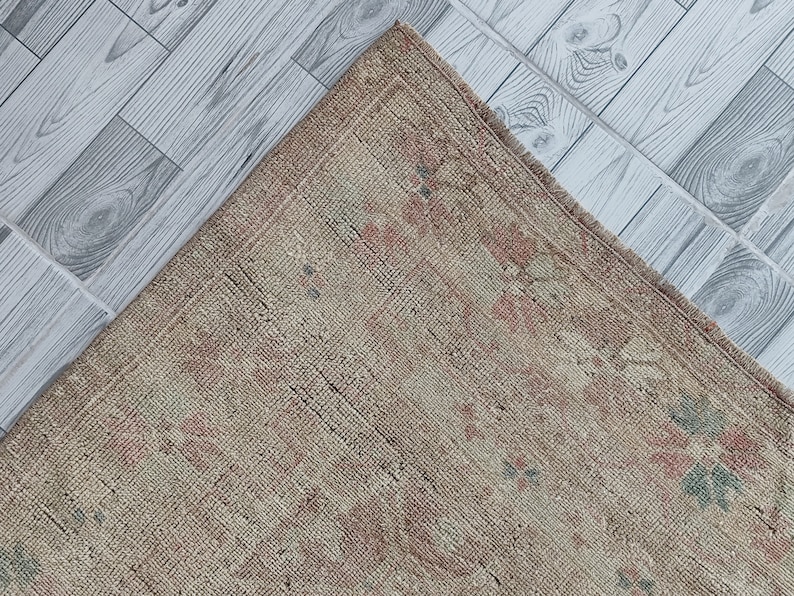 May include: A vintage rug with a faded floral pattern in shades of pink, green, and beige. The rug has a worn, distressed look and is made of a natural fiber.