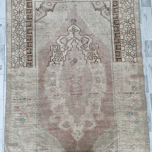 May include: A vintage rug with a faded pink and beige color scheme. The rug has a traditional design with a central medallion and floral motifs. The rug is in good condition with some wear and tear.