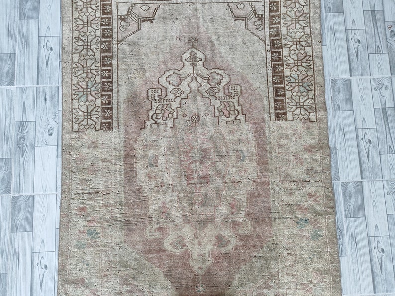 May include: A vintage rug with a faded pink and beige color scheme. The rug has a traditional design with a central medallion and floral motifs. The rug is in good condition with some wear and tear.