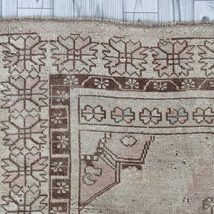 May include: Close-up of a beige rug with a brown and pink geometric pattern. The rug has a fringe border.