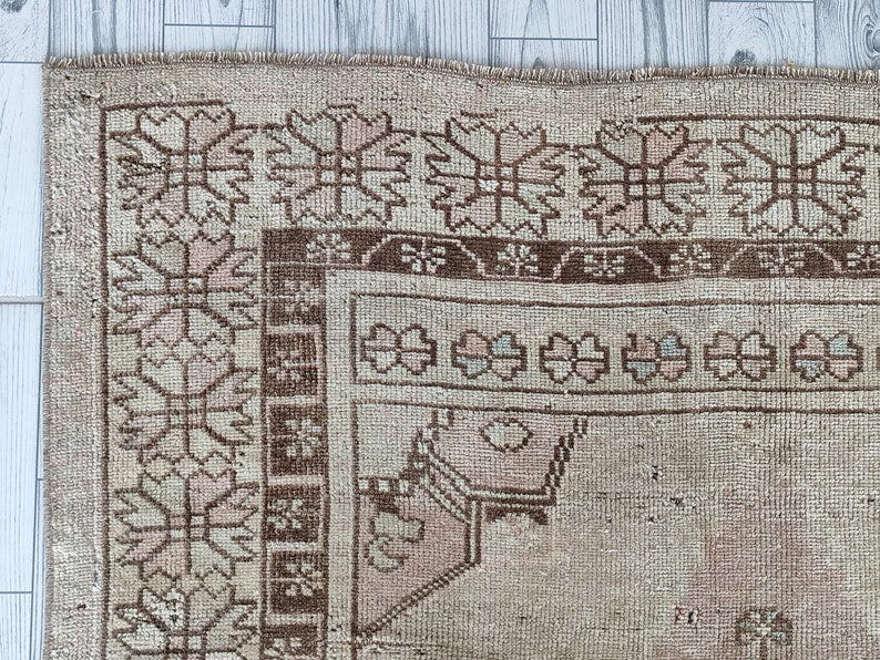 May include: Close-up of a beige rug with a brown and pink geometric pattern. The rug has a fringe border.