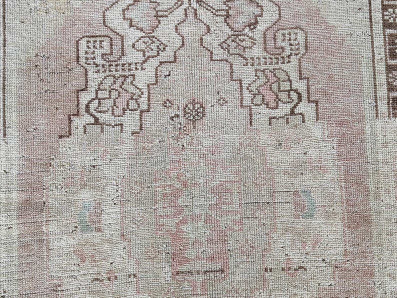May include: A close-up of a white rug with a faded brown geometric pattern. The rug has a worn and distressed look, with some areas showing signs of wear and tear.