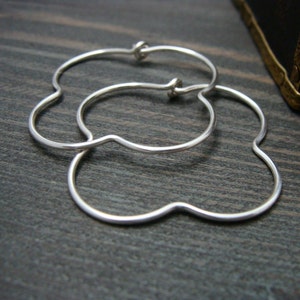 May include: A pair of silver flower-shaped hoop earrings. The earrings are made of thin, smooth metal and have a delicate, feminine design.