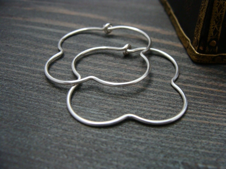 May include: A pair of silver flower-shaped hoop earrings. The earrings are made of thin, smooth metal and have a delicate, feminine design.