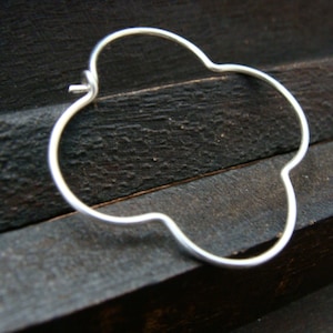 May include: A silver four-leaf clover shaped hoop earring.