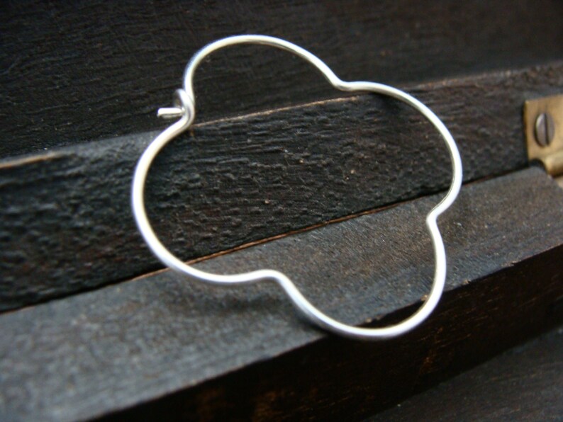 May include: A silver four-leaf clover shaped hoop earring.