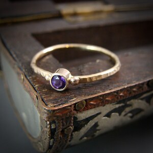 May include: A hammered gold band ring with a single round purple amethyst gemstone.