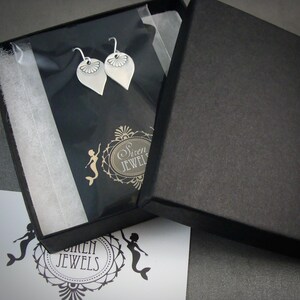 May include: A black box with a white interior, containing two silver earrings with a floral design. The box is open and the earrings are visible. The box has the text "Siren Jewels" printed on it.