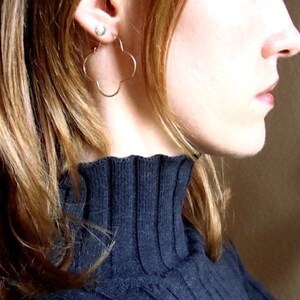 May include: A woman with long, straight, reddish-brown hair wearing a black mock neck sweater. She is wearing a pair of gold clover-shaped hoop earrings.