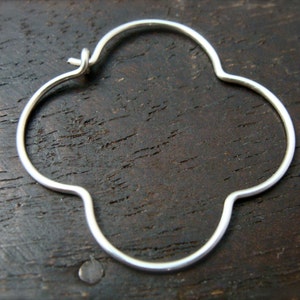 May include: Silver clover-shaped hoop earrings. The earrings are made of a thin, smooth metal and have a simple, elegant design.
