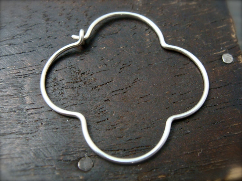May include: Silver clover-shaped hoop earrings. The earrings are made of a thin, smooth metal and have a simple, elegant design.