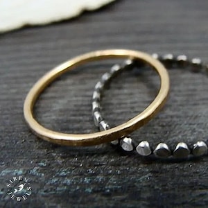May include: Two rings are shown, one with a smooth, polished gold-tone finish and a thin, rounded band, and the other with a textured, dark silver-tone finish featuring a series of small, bead-like segments along the entire circumference of the band.