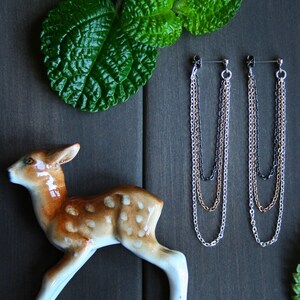May include: A pair of long, dangling earrings with three chains in silver, gold, and black. The chains are layered and hang from a small black bead.