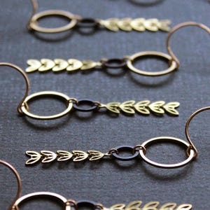 K&ouml;nnte beinhalten: Vier Paar goldene Ohrringe mit schwarzen Akzenten und einem Blattdesign. Die Ohrringe h&auml;ngen an einem Haken.