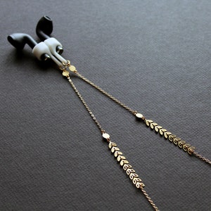 May include: A pair of white and black earbuds with a gold chain attached. The chain has small gold leaf-shaped charms.