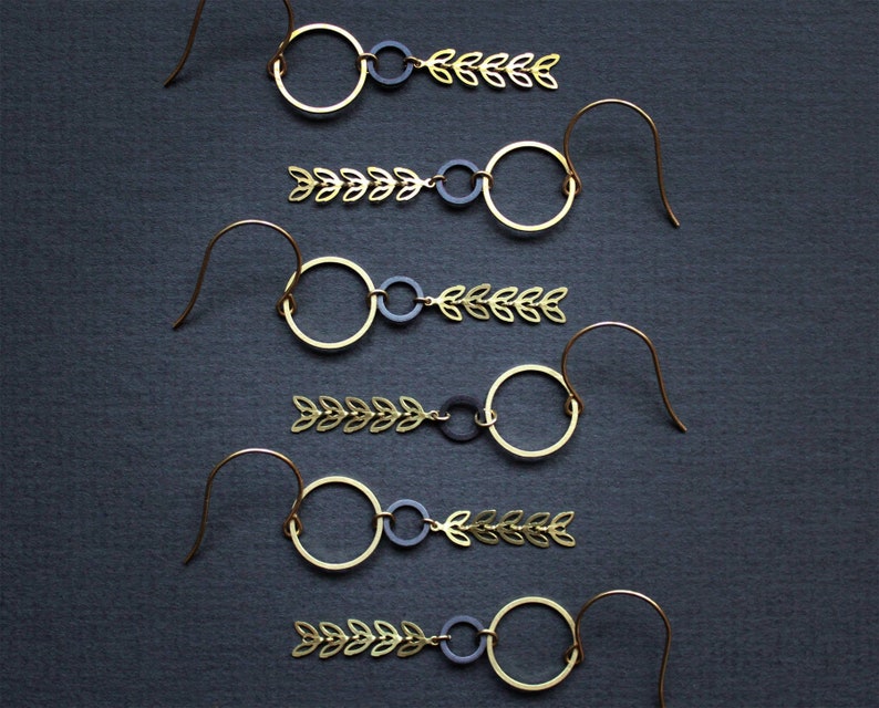 K&ouml;nnte beinhalten: F&uuml;nf Paar goldene Ohrringe mit schwarzen und goldenen Akzenten. Jeder Ohrring hat einen kleinen Kreis mit einem Blattdesign.