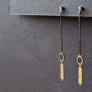 May include: A pair of gold dangle earrings with black chains and leaf-shaped charms. The earrings have a simple, minimalist design.