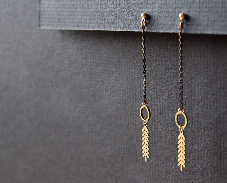 May include: A pair of gold dangle earrings with black chains and leaf-shaped charms. The earrings have a simple, minimalist design.