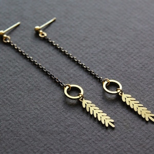 May include: A pair of gold dangle earrings with a black chain and a leaf design. The earrings have a small circle at the top and a long, thin chain that ends in a leaf-shaped pendant.