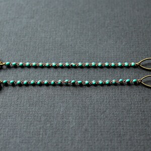 May include: Two gold leaf-shaped charms attached to a turquoise beaded chain with gold metal loops and clear plastic ends. This is a glasses chain.