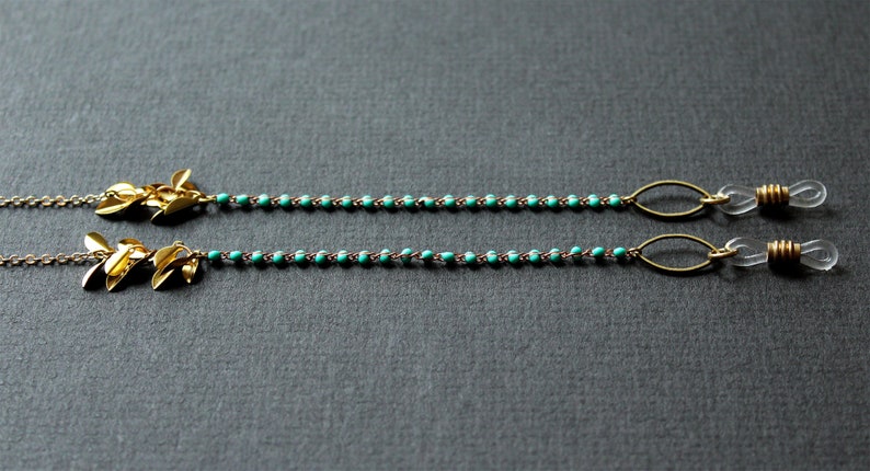 May include: Two gold leaf-shaped charms attached to a turquoise beaded chain with gold metal loops and clear plastic ends. This is a glasses chain.