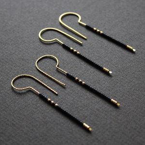 May include: Three pairs of gold hoop earrings with black beaded strands hanging from them.