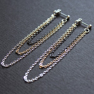 May include: Two pairs of chain earrings with three chains in each pair. The chains are silver, gold, and black.