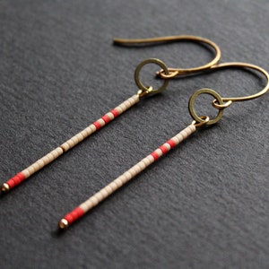 May include: A pair of long, beaded earrings with a gold hoop at the top. The beads are cream and red, creating a striped pattern.