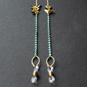 May include: A pair of gold-toned eyeglass chains with turquoise beads and gold leaf accents. The chains are attached to clear plastic eyeglass holders.