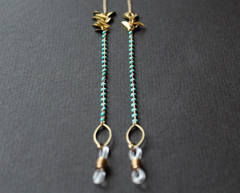 May include: A pair of gold-toned eyeglass chains with turquoise beads and gold leaf accents. The chains are attached to clear plastic eyeglass holders.