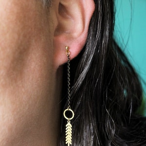May include: Gold leaf earrings with a black chain and a small gold circle. The earrings are hanging from the earlobe.