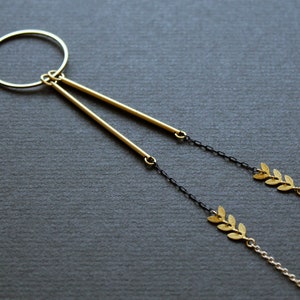 May include: A gold necklace with a circle pendant and two dangling gold bars. The necklace has a black chain with gold leaf accents.