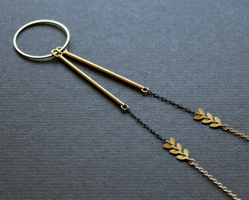 May include: A gold necklace with a circle pendant and two dangling gold bars. The necklace has a black chain with gold leaf accents.