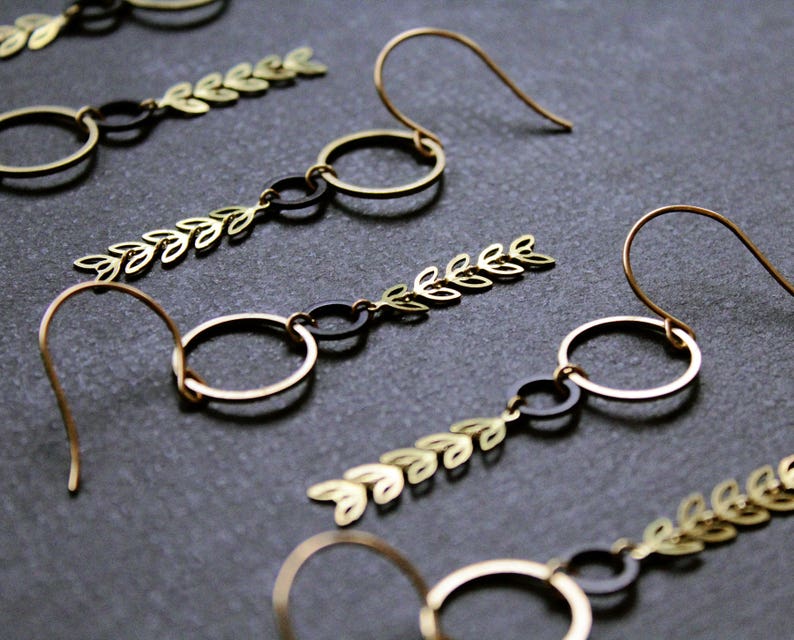 K&ouml;nnte beinhalten: Goldene und schwarze Ohrringe mit einem Blattdesign und mehreren Kreisen.
