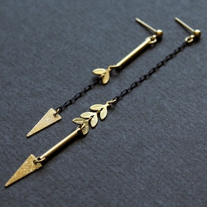 May include: A pair of gold earrings featuring a delicate leaf design and a triangular shape at the bottom. The earrings are suspended from a black chain.