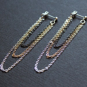 May include: A pair of gold, silver, and black chain earrings. The earrings are made of three chains of different colors, and they are connected to a small silver bar.