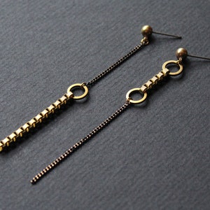 May include: A pair of long gold chain earrings with black chain accents. Each earring features a small gold circle and a longer chain with a series of small gold squares.