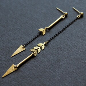 May include: A pair of gold earrings with a delicate leaf design and a triangle shape at the bottom. The earrings are suspended from a black chain.