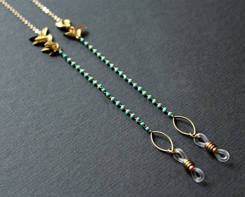 May include: Gold eyeglass chain with turquoise beads and leaf-shaped charms. The chain has two gold loops at the ends for attaching to glasses.