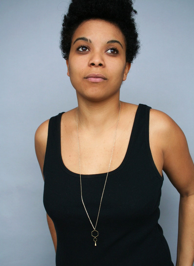 May include: A person wearing a black tank top with a gold chain necklace featuring a geometric pendant.