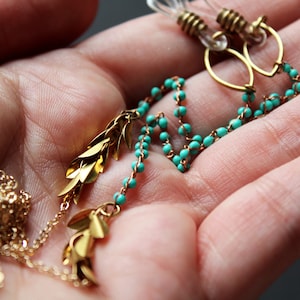 May include: Gold and turquoise beaded earrings with leaf-shaped charms hanging from the bottom.