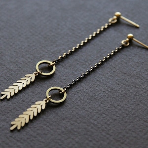 May include: A pair of long, delicate earrings with a black chain and gold leaf and circle accents.