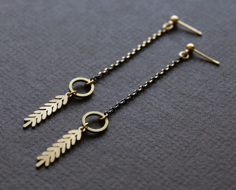 May include: A pair of long, delicate earrings with a black chain and gold leaf and circle accents.