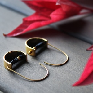 May include: A pair of gold hoop earrings with black accents. The earrings are made of a thin metal and have a simple design.